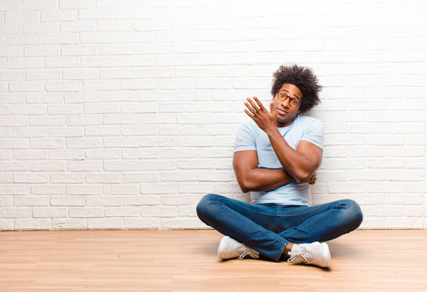 young black man feeling confused and clueless, wondering about a doubtful explanation or thought sitting on the floor at home - Foto, afbeelding