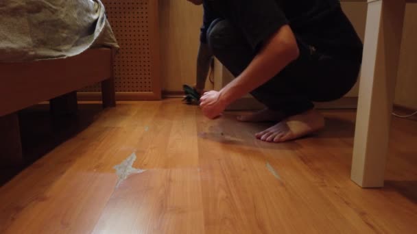 Młody człowiek myje podłogę w domu. Zbliżenie mężczyzny wycierającego brud z drewnianej podłogi specjalną szmatką. - Materiał filmowy, wideo