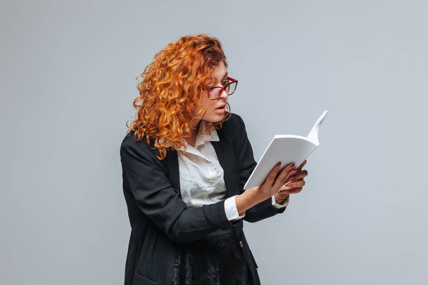 Red-haired girl in a jacket surprised by the book - Photo, Image