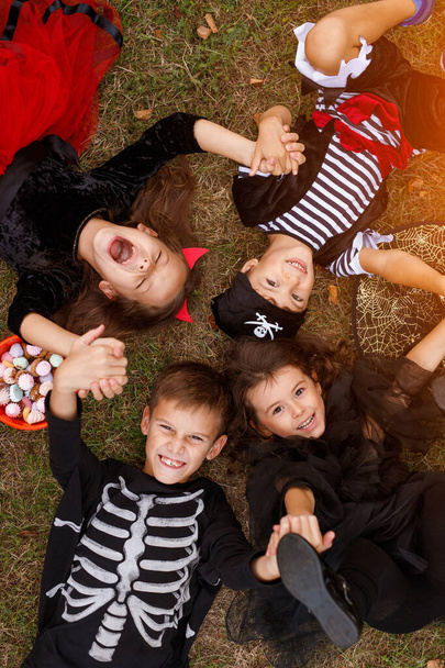 Ευτυχισμένα παιδιά με αποκριάτικες στολές ξαπλωμένα στο γρασίδι - Φωτογραφία, εικόνα