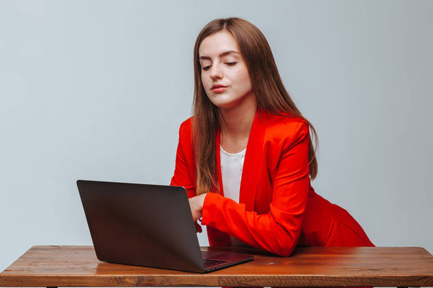 Girl in a red jacket with a laptop at the table light background - Photo, image