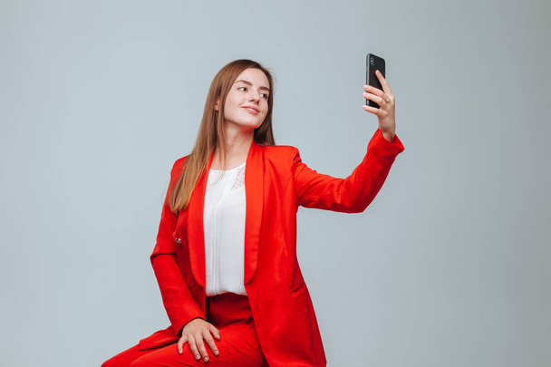 girl in a red jacket takes a selfie on the phone on a gray backg - Foto, immagini
