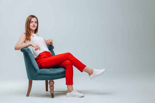 Mädchen in roter Hose sitzt auf einem Stuhl vor hellgrauem Hintergrund - Foto, Bild
