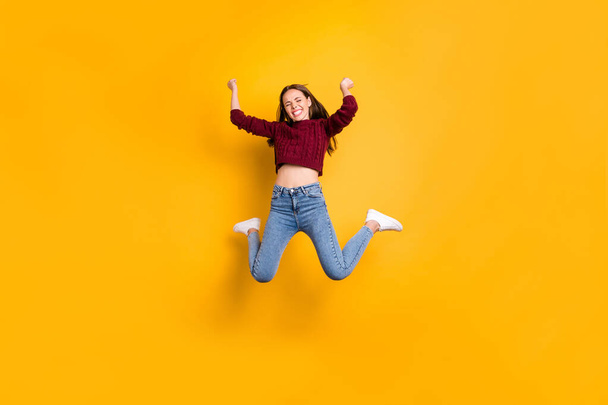 Full length photo of delighted woman with her closed eyes and long haircut raising fists wearing burgundy sweater isolated over yellow background - 写真・画像