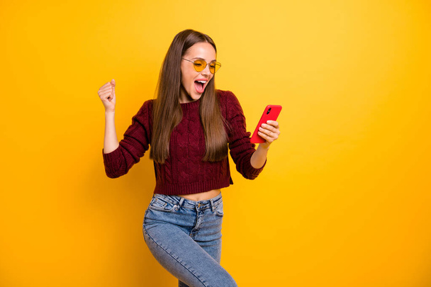 Portrait of crazy youth in eyewear eyeglasses raising her screaming yeah wearing denim jeans maroon jumper isolated over yellow background - Foto, imagen