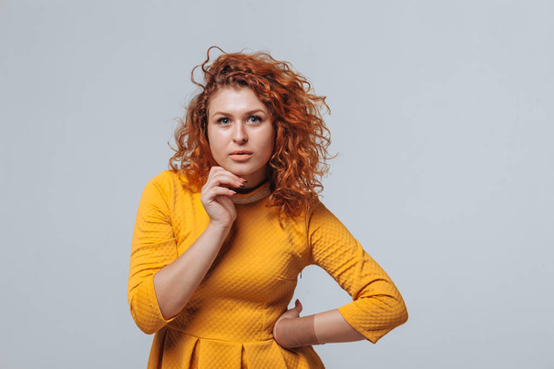 Redhaired curly girl Thinks on a light gray background - Foto, Bild