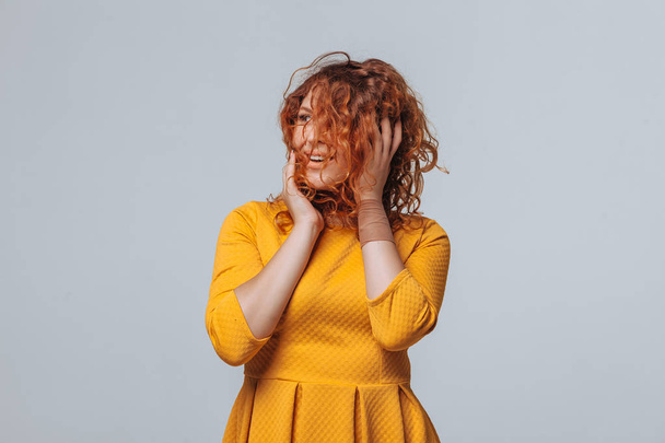 Cheerful red curly girl in a yellow dress on a light gray backgr - Photo, Image