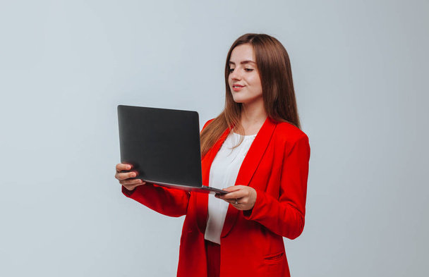 κορίτσι σε ένα κόκκινο μπουφάν κρατά ένα φορητό υπολογιστή σε ελαφρύ φόντο - Φωτογραφία, εικόνα