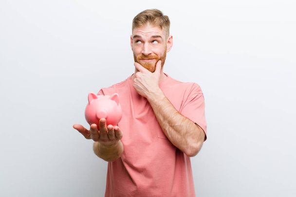 young red head man holding a piggy bank against white background - Foto, immagini
