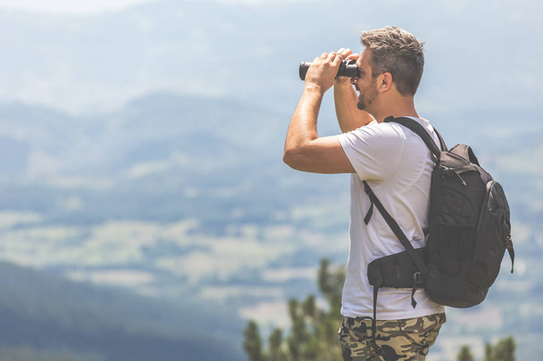 Traveler with backpack standing on the top of the mountain and using binoculars - Фото, зображення