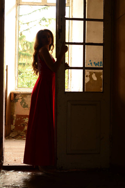 beautiful girl in red dress posing in the room of the abandoned house - Photo, image