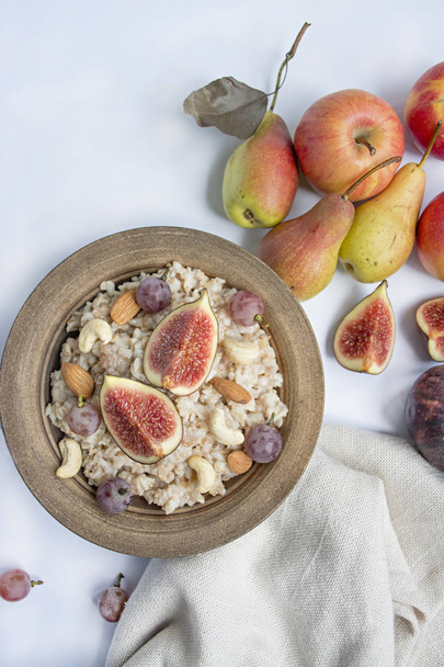 Oatmeal in a bowl with fresh figs, almonds and cashews. Oatmeal with fruits. White background. - Foto, Imagem
