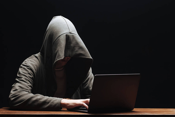 Hacker en una capucha con un portátil sobre un fondo negro
 - Foto, Imagen