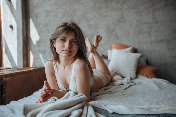 Schattig meisje liggend in de ochtend op het bed in wit linnen - Foto, afbeelding