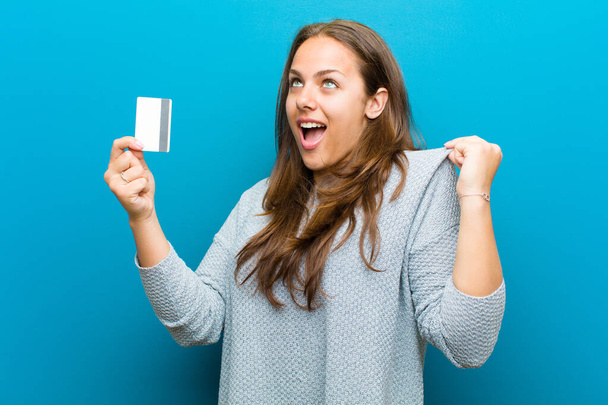 young woman with a credit card against blue background - Foto, imagen