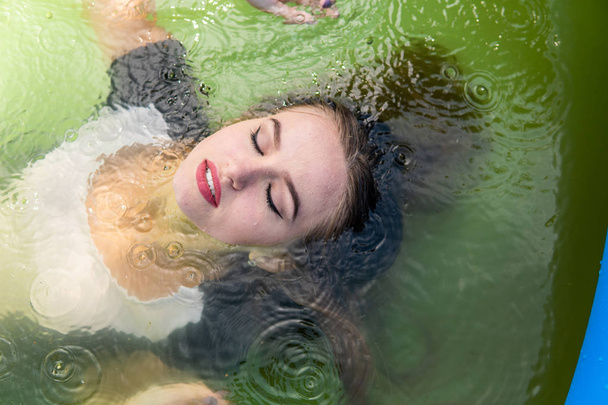 Krásná modelka oblečený v dlouhých večerních šatů, leží v bazénu a smyslně představuje - Fotografie, Obrázek