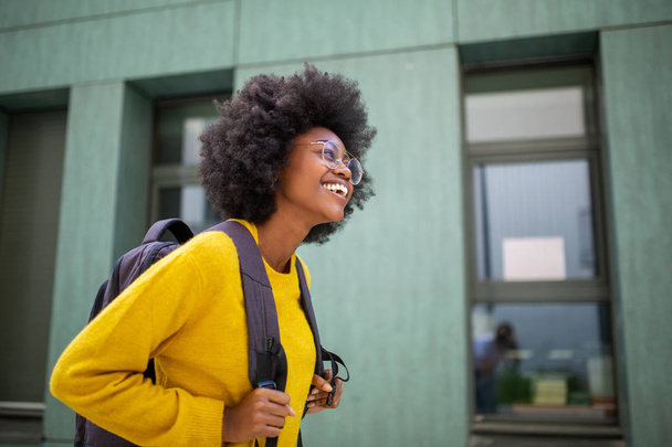 Side portrait of happy black female college student with glasses and bag - Photo, image