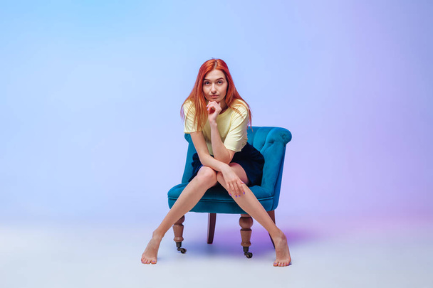 Ragazza dai capelli rossi con belle gambe lunghe seduta su una sedia
 - Foto, immagini