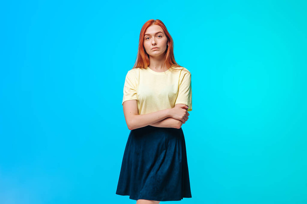 serious red-haired girl crossed her arms over her chest on a blu - 写真・画像