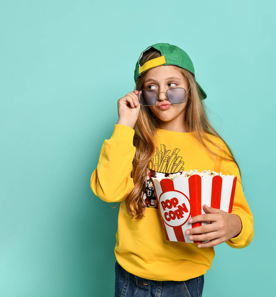 Young cute woman eating popcorn over green background. - Foto, immagini