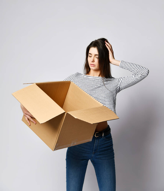 beautiful brunette woman standing on a light background with a moving cardboard box - Zdjęcie, obraz