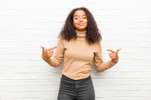 young black woman looking proud, arrogant, happy, surprised and satisfied, pointing to self, feeling like a winner against brick wall - Foto, Bild