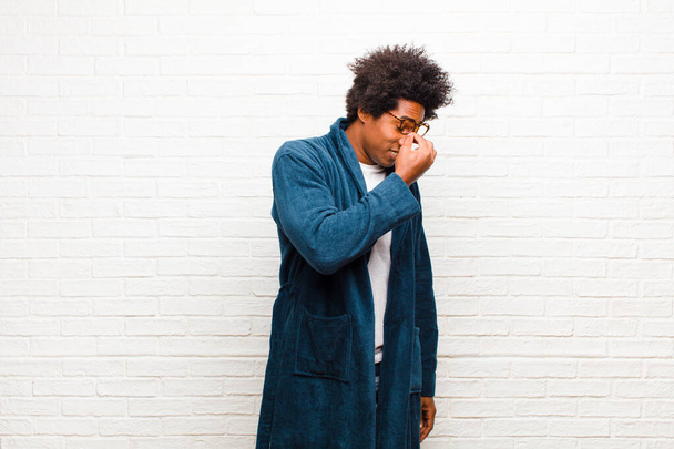 young black man wearing pajamas with gown feeling stressed, unhappy and frustrated, touching forehead and suffering migraine of severe headache against brick wall - Fotografie, Obrázek