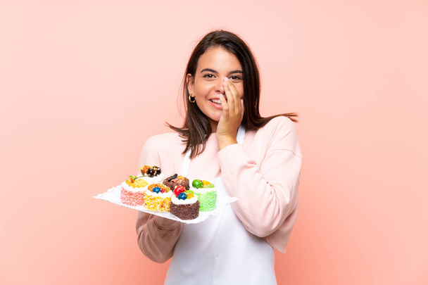 Giovane ragazza che tiene un sacco di diverse mini torte su sfondo isolato con espressione facciale a sorpresa
 - Foto, immagini