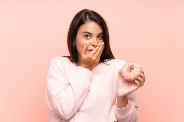 Young girl holding a donut over isolated pink background with surprise facial expression - Photo, Image