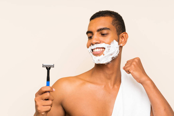 Young handsome man shaving his beard over isolated background celebrating a victory - Fotó, kép