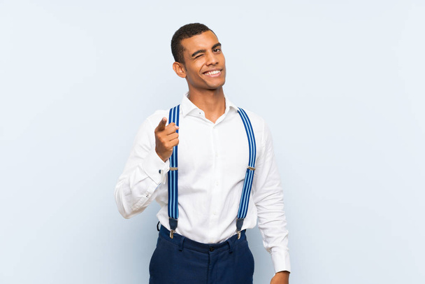 Young handsome brunette man with suspenders over isolated background points finger at you - 写真・画像