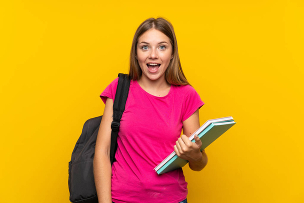 jong student meisje over geïsoleerde gele achtergrond met verrassing en geschokt gezichtsuitdrukking - Foto, afbeelding