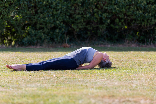 Egy középkorú nő, aki mezítláb jógázik egy füves parkban. - Fotó, kép