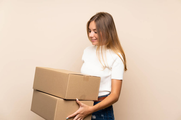 Молодая блондинка на изолированном фоне держит коробку, чтобы переместить ее на другой сайт
 - Фото, изображение