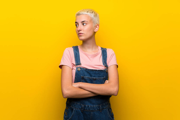 Teenager girl with overalls on yellow background portrait - Photo, Image