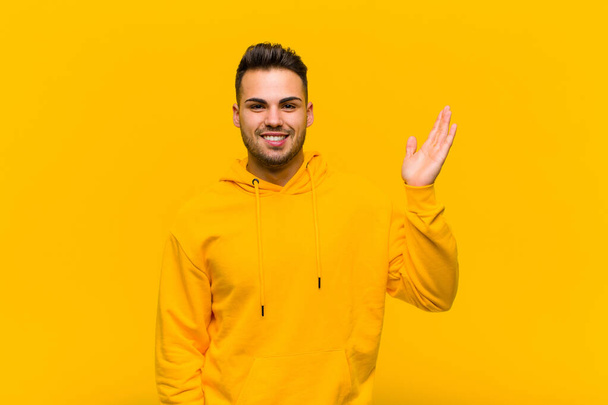 young hispanic man feeling happy, surprised and cheerful, smiling with positive attitude, realizing a solution or idea against orange wall - Foto, Imagen