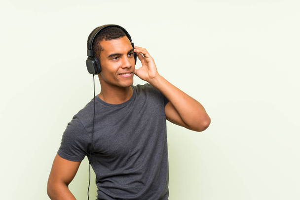 junger gutaussehender Mann hört Musik mit Handy über isolierte grüne Mauer - Foto, Bild