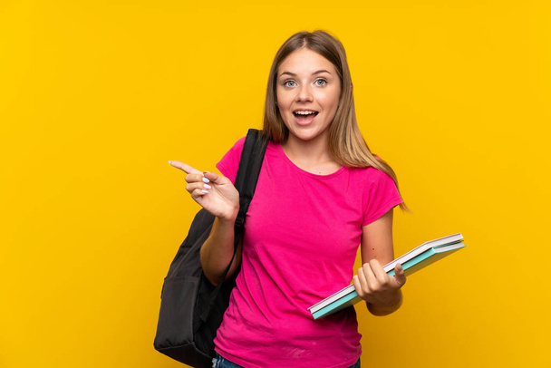 Young student girl over isolated yellow background surprised and pointing finger to the side - Photo, Image