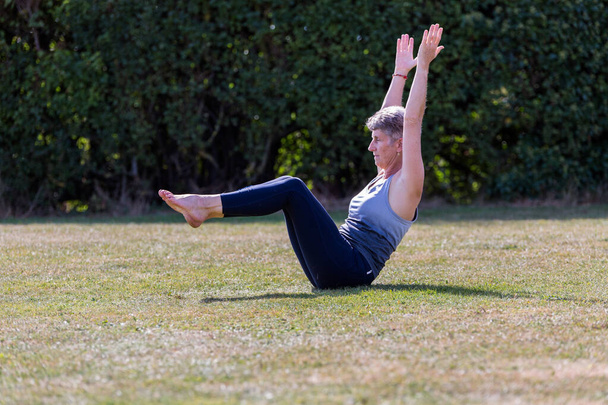 Kobieta w średnim wieku uprawiająca jogę boso na zewnątrz w trawiastym parku - Zdjęcie, obraz