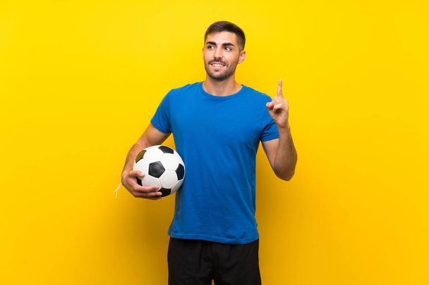Jeune beau joueur de football homme sur mur jaune isolé dans l'intention de réaliser la solution tout en levant le doigt
 - Photo, image