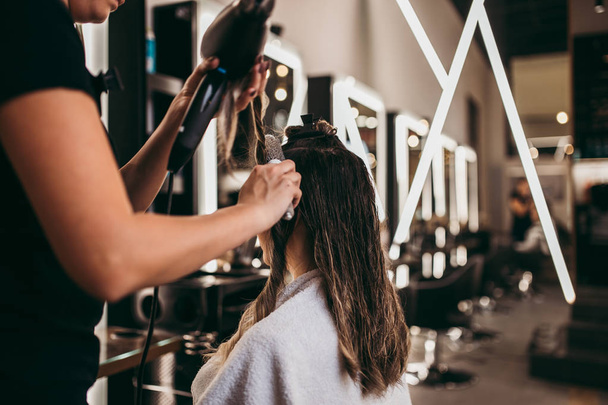 Beautiful brunette woman with long hair at the beauty salon getting a hair blowing. Hair salon styling concept. - Photo, image