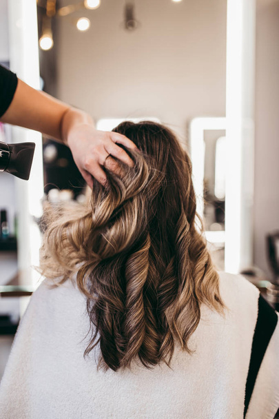 Beautiful brunette woman with long hair at the beauty salon getting a hair blowing. Hair salon styling concept. - Fotoğraf, Görsel