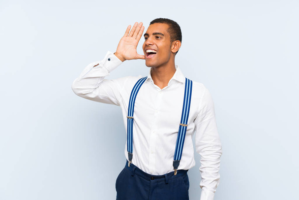 Young handsome brunette man with suspenders over isolated background shouting with mouth wide open - Photo, Image