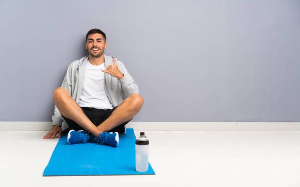 Sport man sitting one the floor making phone gesture - Foto, afbeelding
