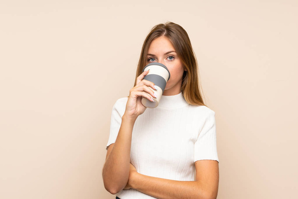 Giovane donna bionda su sfondo isolato che tiene e beve un caffè da portare via
 - Foto, immagini