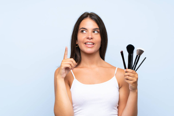 Young girl holding a lot of makeup brush intending to realizes the solution while lifting a finger up - Foto, Imagem