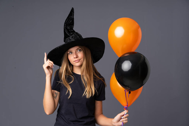 Siyah ve turuncu hava balonları tutan genç cadının şüpheleri ve kafa karıştırıcı bir yüz ifadesi var. - Fotoğraf, Görsel