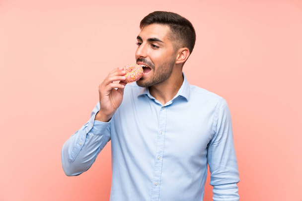 Young man holding a donut over isolated pink background - Foto, Imagen
