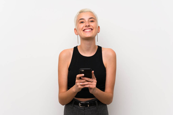 Chica adolescente con el pelo corto sobre la pared blanca enviando un mensaje con el móvil
 - Foto, imagen