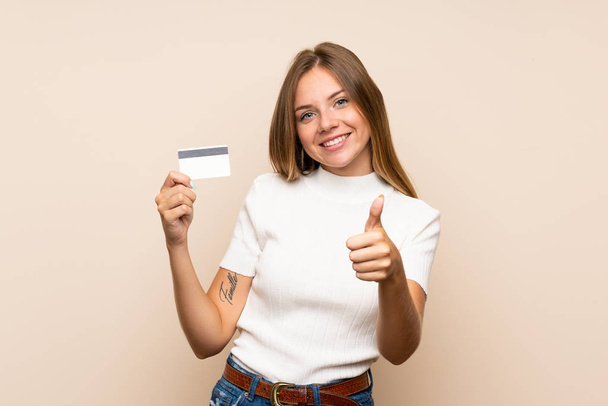 junge blonde Frau mit isoliertem Hintergrund mit Kreditkarte - Foto, Bild